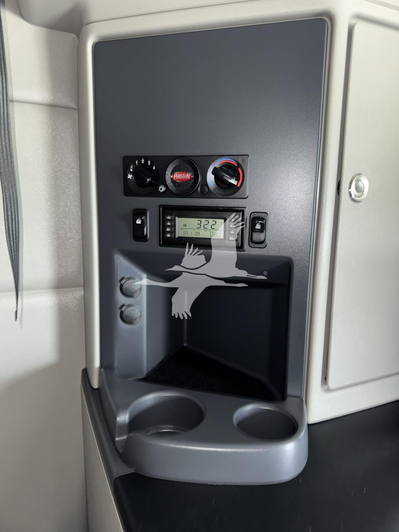 Peterbilt 579 cab interior showing controls dashboard with gauges and a small display, cup holder and storage area.