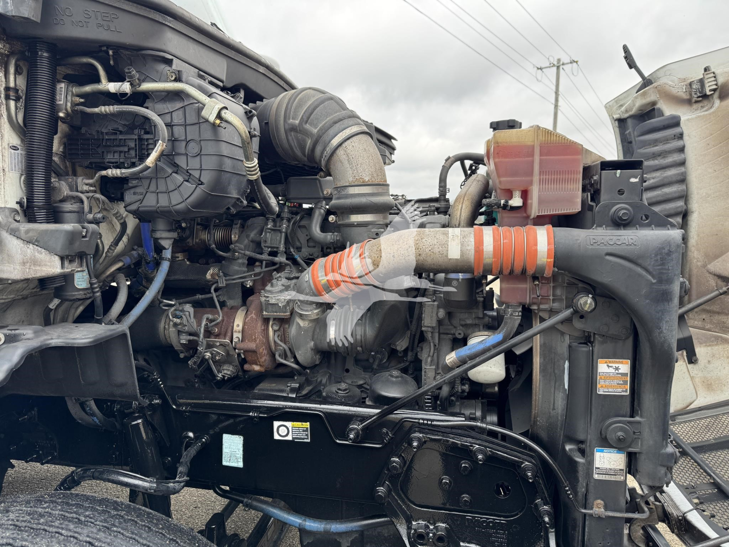 Peterbilt 579 engine bay showing turbocharger, intercooler piping, coolant reservoir, alternator, and various hoses in view.
