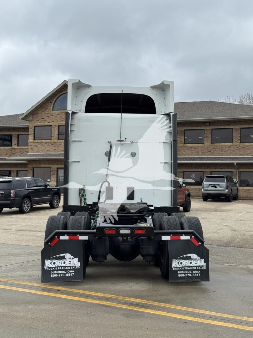 Peterbilt 579 semi-truck rear view showing sleeper cab, taillights, rear bumper with mudflaps, and attached fifth wheel in a dealership parking lot.