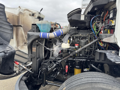 Peterbilt 579 engine bay view with exposed components including wiring harnesses, hoses, and hydraulic lines; visible belt tensioner and air intake; engine block in view.