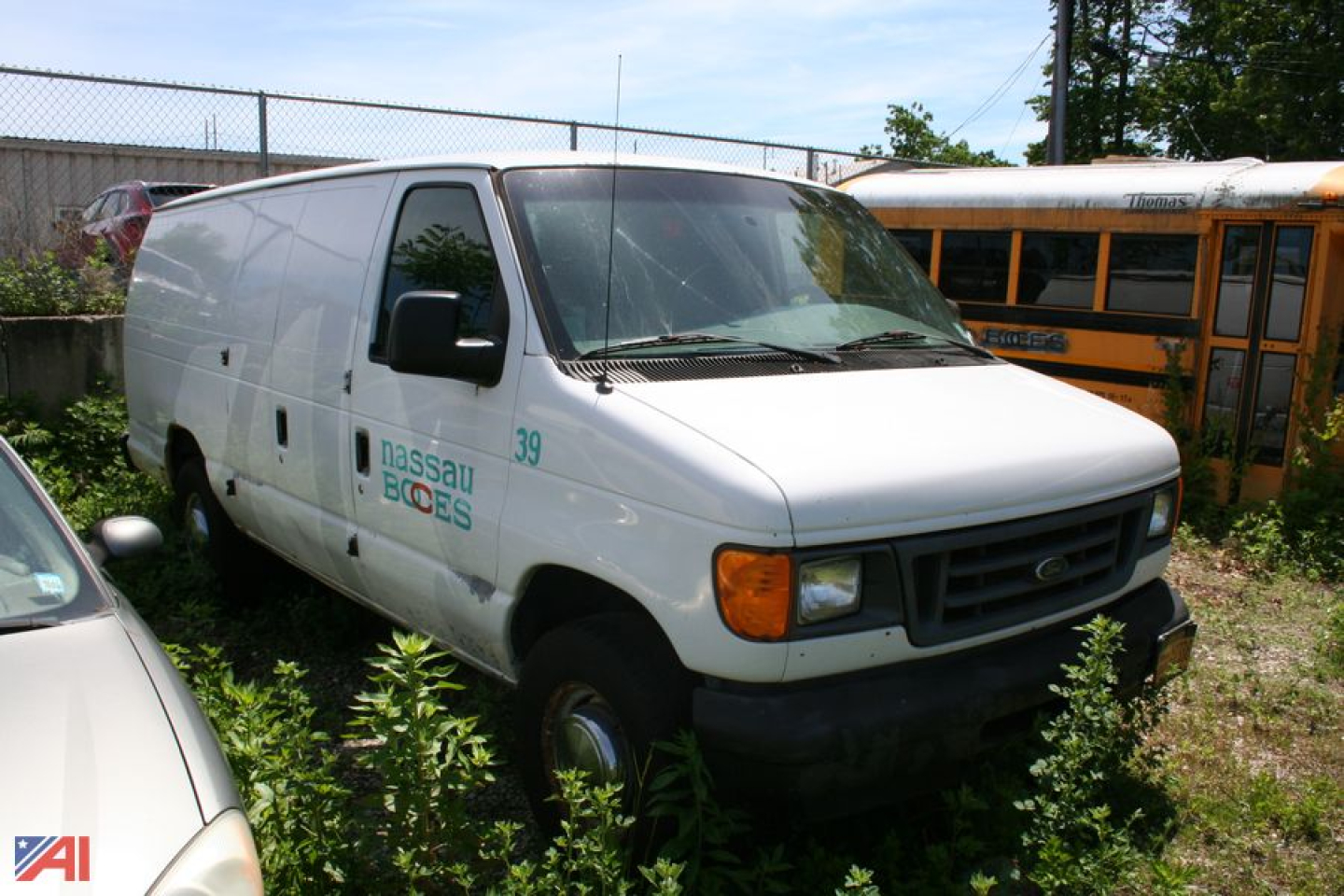 Ford E-Series cargo van with Nassau BOCES logo on side, white exterior, front view, in a lot with a yellow school bus in background.