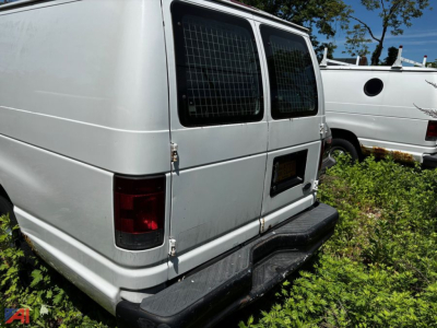 Ford E-Series cargo van rear view showing back doors, rear bumper, and windows with metal grid. White color with hinge hardware on doors.