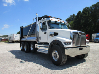 Side view of a white 2027 Western Star 49X dump truck with a large chrome grille, three-axle configuration, and dump bed in a gravel lot.
