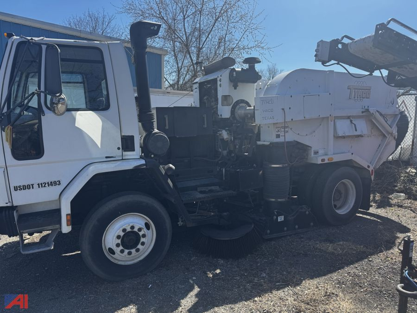 Front-left side of a white Freightliner FC70 sweeper truck with a large spraying/ sweeping unit mounted behind the cab. Visible labels include USDOT 1121439 on the door and model branding on the sweep unit.