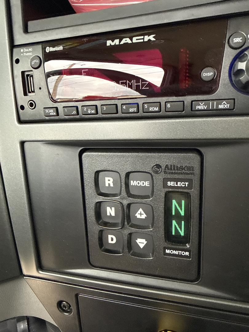 Mack GR64B dash area with transmission gear selector showing N modes and monitor switch; dashboard display visible.