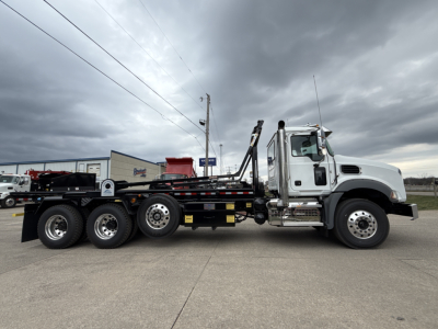 2026 Mack GR64B roll-off truck side view showing cab, long chassis, wheel configuration with six rear wheels, loading arms, and hydraulic components.