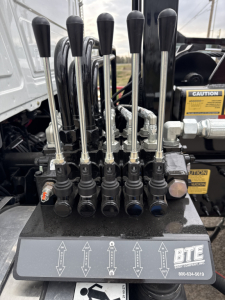 Control levers and hydraulic control unit on Mack GR64B roll-off truck showing multiple black handles and labeled indications.