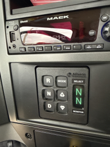 Mack GR64B dash area with transmission gear selector showing N modes and monitor switch; dashboard display visible.