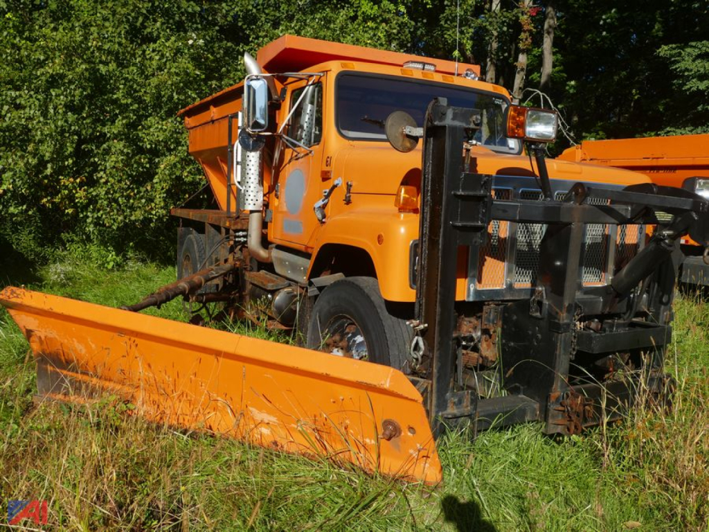 Orange International 2574 truck with front plow attachment and snowplow blade, side view in grassy lot.