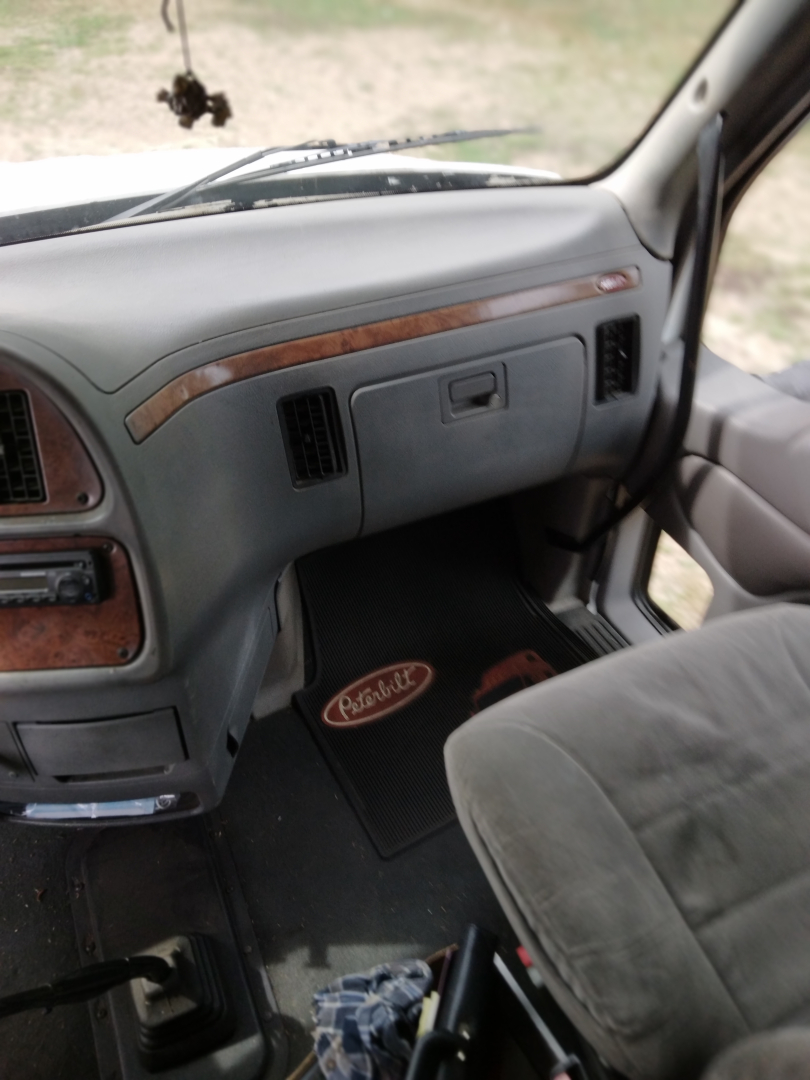 Peterbilt truck dashboard and passenger seat area with wood trim, A/C vents, and Peterbilt floor mat