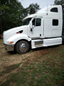 2005 Peterbilt 387 conventional sleeper truck side view showing white cab, chrome front bumper, dual fuel tanks, and sleeper cabin window.