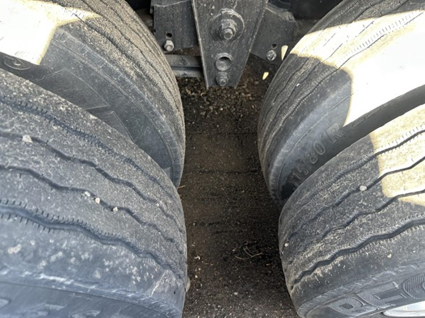 Dual rear trailer tires with mud and dirt, undercarriage visible, part of a flatbed trailer frame near the hitch area.