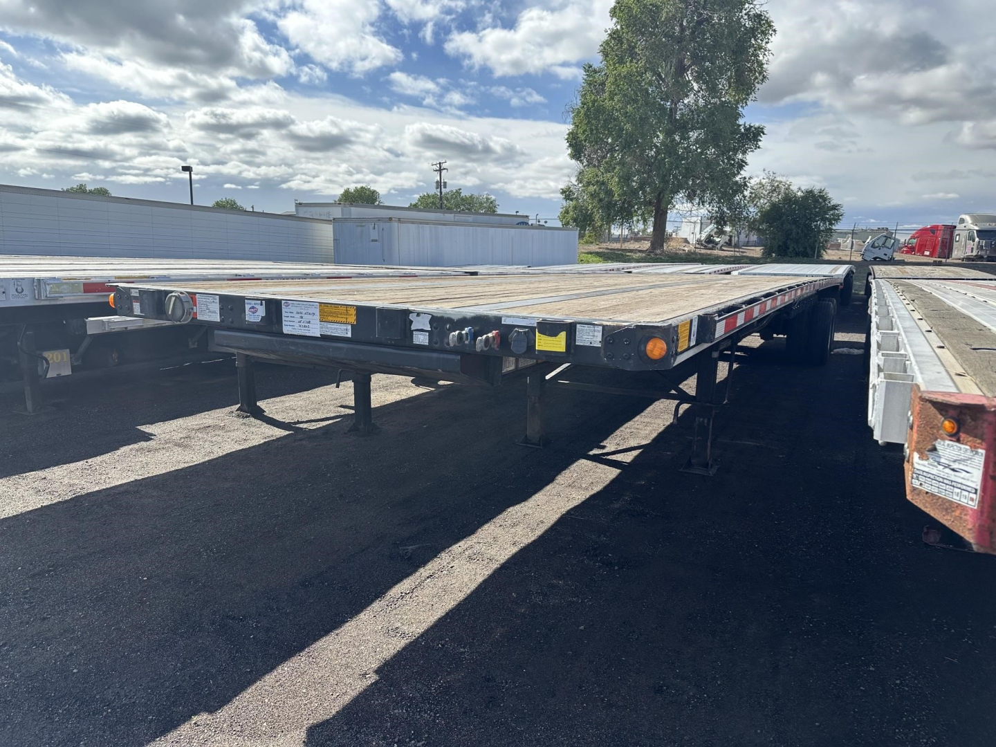 Flatbed trailer with loading deck showing side reflectors and rear lights; utility steel flatbed trailer in use, long platform, undercarriage visible