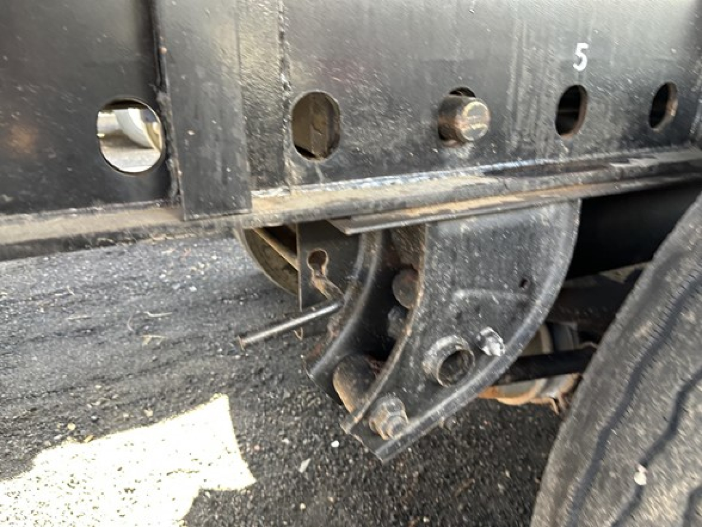 Flatbed trailer wheel assembly and frame showing mounting bracket and springs with perforated steel side rail.