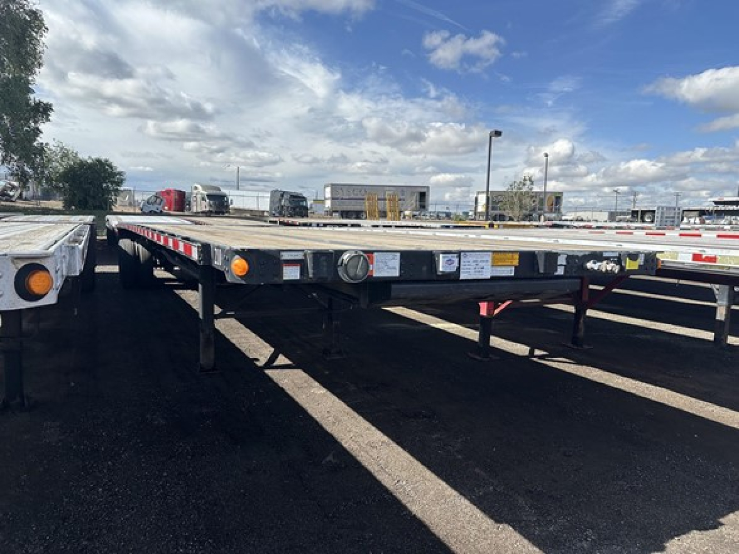 Flatbed trailer in a used inventory lot showing reflective tape, marker lights, and support legs.