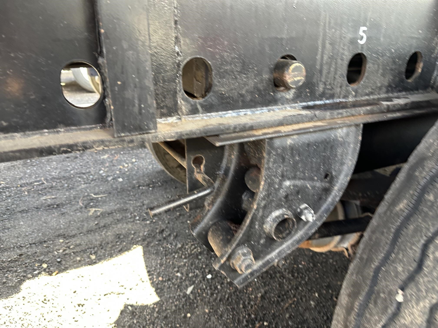 Trailer frame with mounting brackets and a curved custom hitch/brace showing holes labeled with numbers on a steel flatbed trailer side.