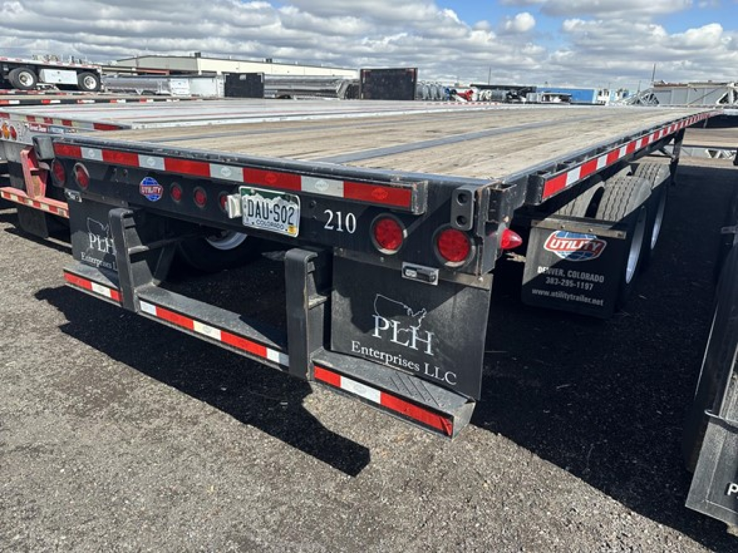 Utility Steel flatbed trailer rear view showing wood deck, red/white reflective tape, taillights, and mudflaps with PEH Enterprise LLC logo. License plate area and number 210 visible.
