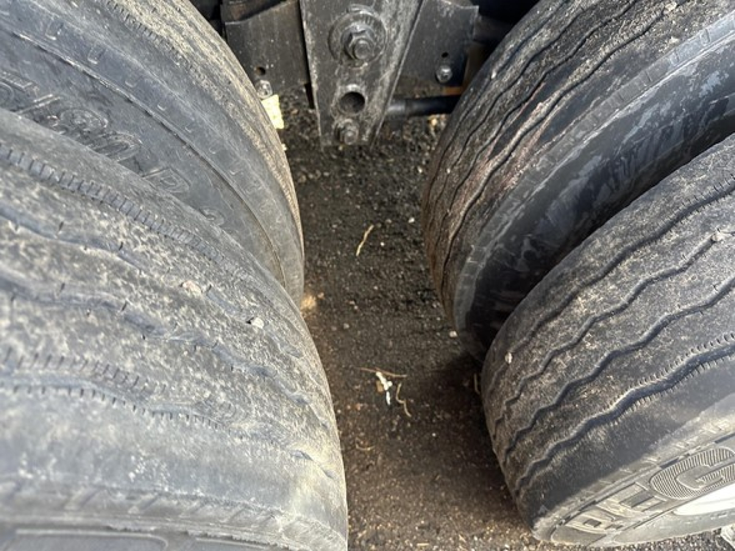 Flatbed trailer wheels (dual axles) with worn tread and dirt, undercarriage visible.