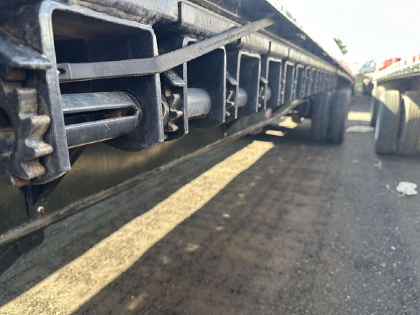 Trailer undercarriage close-up showing interchangeable stake pockets and underframe components of a flatbed trailer.