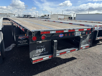 Flatbed trailer showing wooden deck with red/white reflective tape, rear fenders and PLH Enterprises LLC mudflaps, utility logo, two tail lights per side, and Idaho or Utah license plate area.