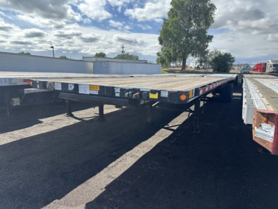 Flatbed trailer in a yard showing rear and side with lights and labels.