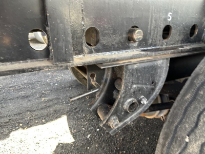 Flatbed trailer wheel assembly and frame showing mounting bracket and springs with perforated steel side rail.