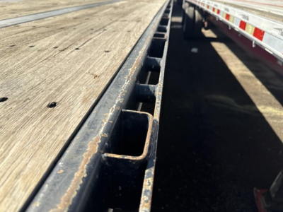 Flatbed trailer edge with wooden deck and metal stake pockets showing wear.