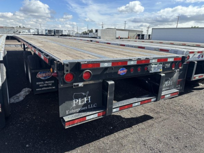 Utility Steel flatbed trailer rear view showing wooden deck, red and white reflective tape, and PHH Enterprises LLC mud flaps.