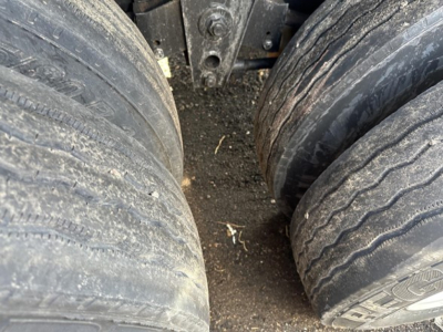 Flatbed trailer wheels (dual axles) with worn tread and dirt, undercarriage visible.
