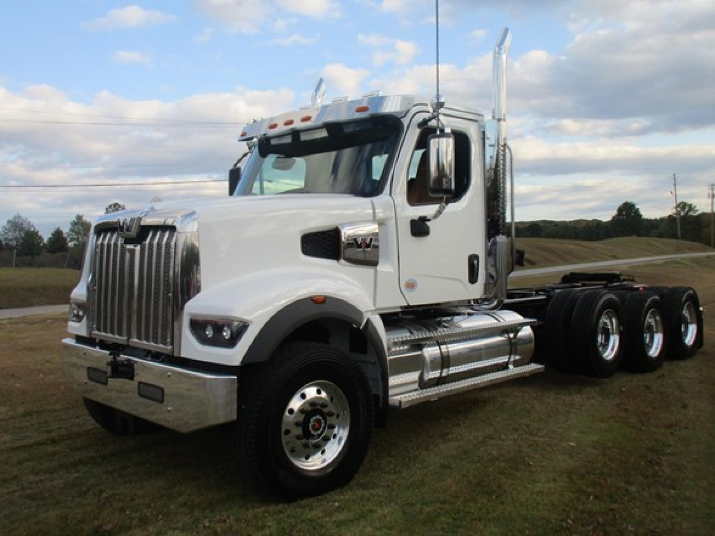 White Western Star 49X day cab truck with chrome bumper and dual rear axles, parked on grass under blue sky.