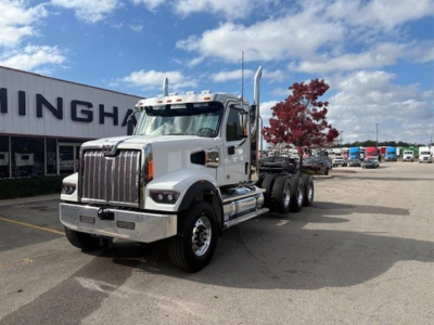 Western Star 49X day cab truck in a dealership lot, chrome grille, single-axle front, daylight, blue sky, trees in background.