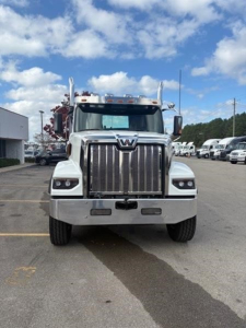 Front view of a white 2026 Western Star 49X truck, chrome grille, large bumper, dual mirrors, clear sky with clouds, dealership lot in background.