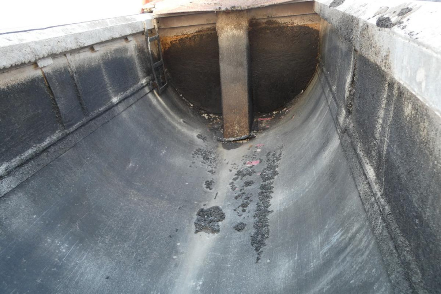Dump truck bed interior showing wear marks and ribbed floor with dark residue and raised center divider.