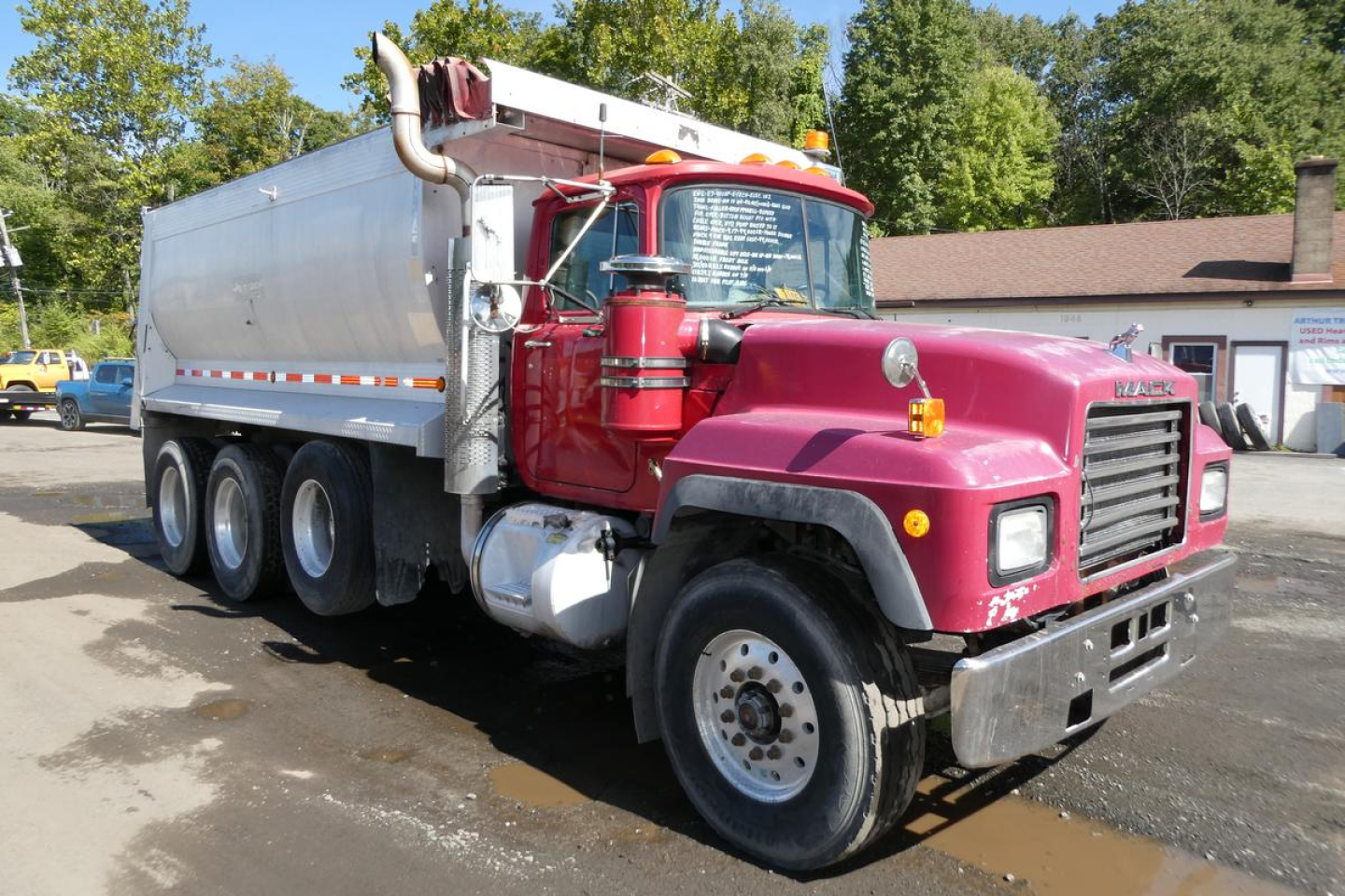 Dump truck showing 2000 Mack RD688S with magenta cab and silver dump body, front grille and dual rear axles.