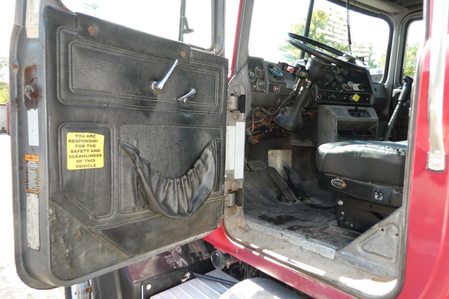 Truck cab interior of a 2000 Mack RD688S dump truck showing driver seat and dashboard, with open door and entry step.