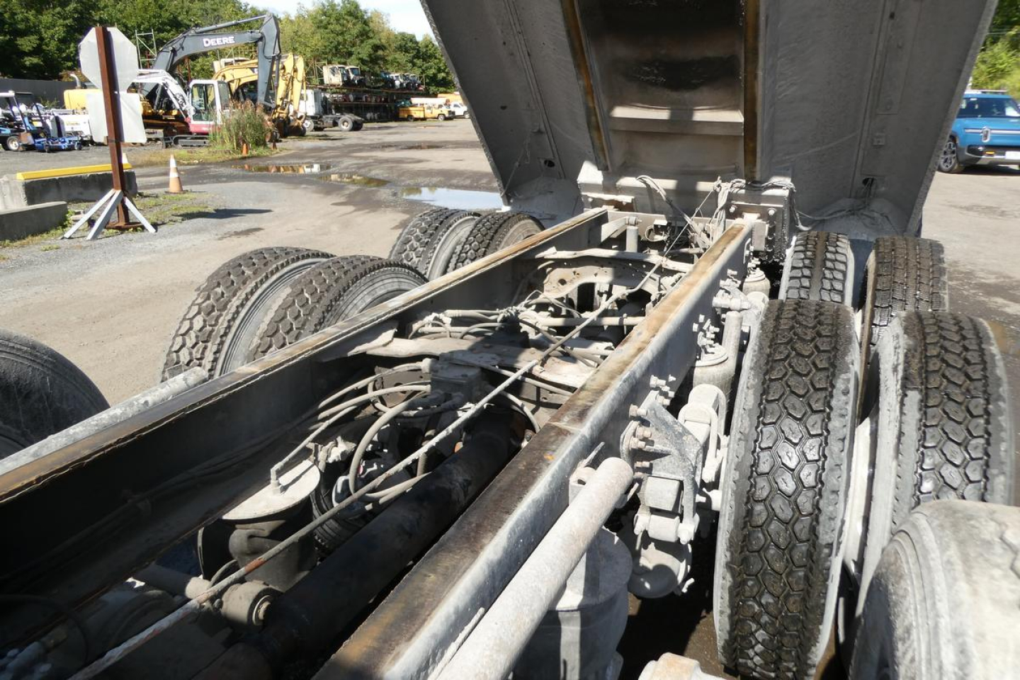 Truck chassis and dump bed area showing dual rear axles and suspension components with hydraulic rams and undercarriage. No legible brand text visible from this angle.