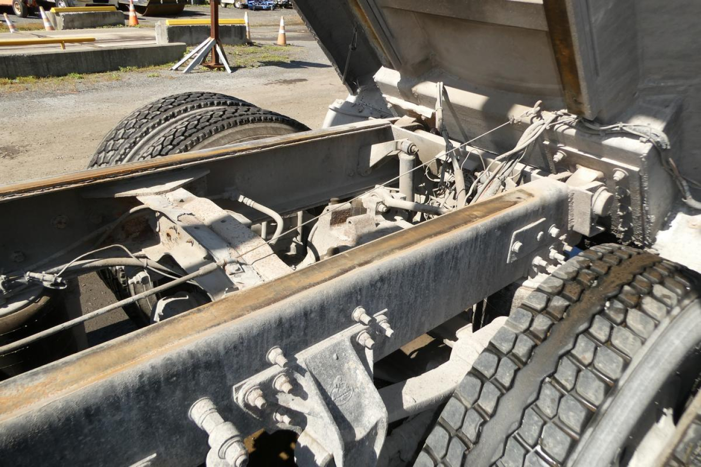 Dump truck chassis and dump bed hinge area showing heavy-duty frame and axles under a Mack RD688S.