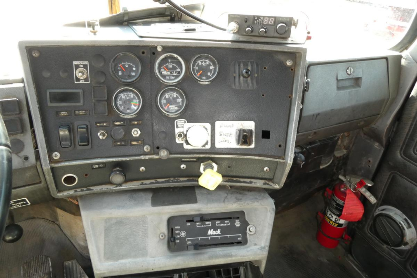 Dashboard interior of a Mack RD688S dump truck showing gauge cluster, switches, ignition, and a red fire extinguisher nearby.