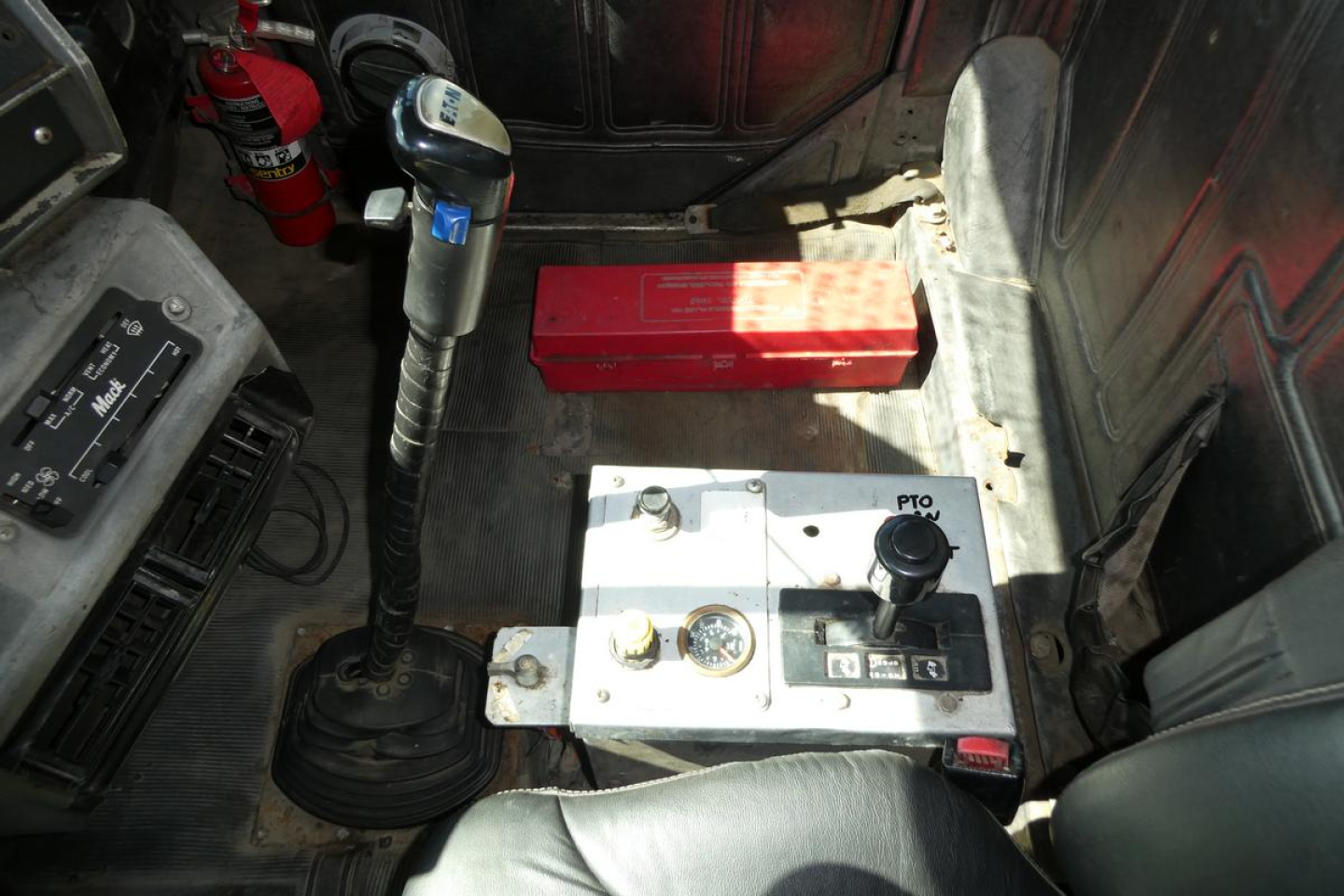 Mack RD688S truck interior showing gear shifter, red toolbox, and metal floor with controls and battery box.