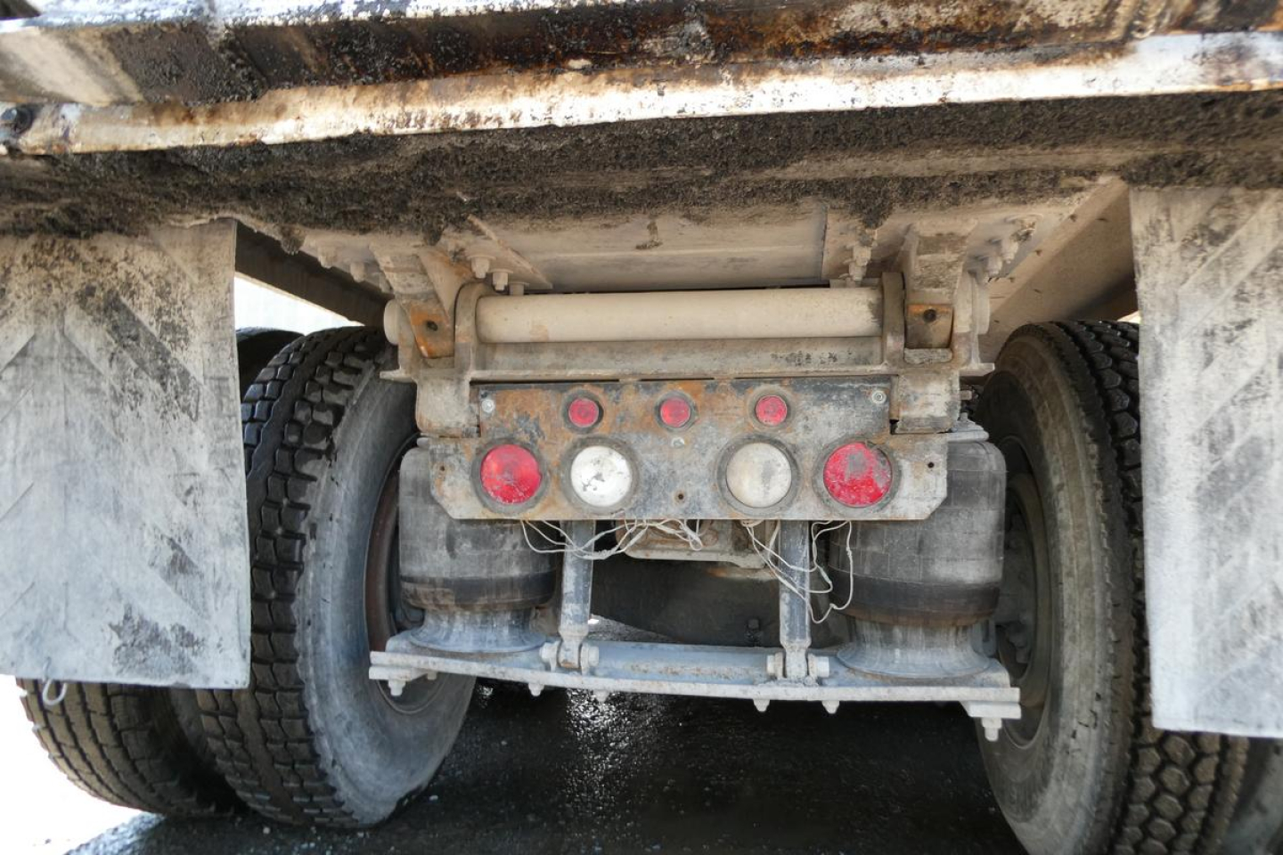 Rear view of Mack RD688S dump truck showing drivetrain, tandem axle suspension, and mud flaps with dirty undercarriage. Visible components include taillights and hydraulic hoses undercarriage.