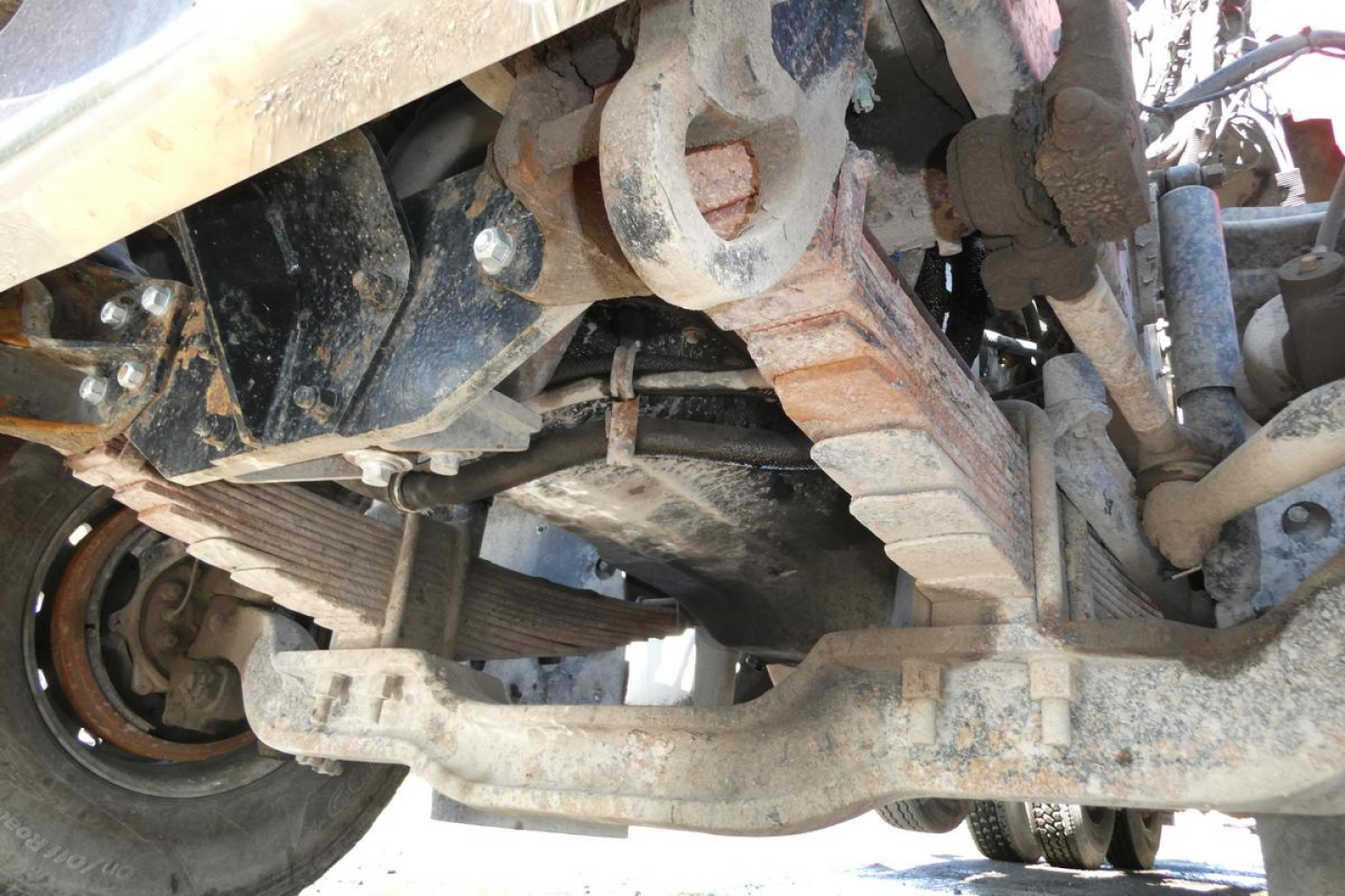Underbody view of a Mack RD688S dump truck showing suspension, frame, driveline, and rust-colored dirt; visible parts include leaf spring, drive shaft, and wheel hub.