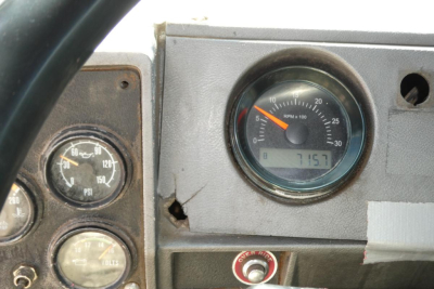 Difficult to read dashboard of 2000 Mack RD688S showing RPM gauge and a digital readout at about 715? with surrounding gauges and key switch plate.