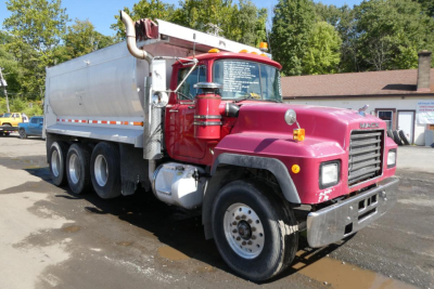Dump truck showing 2000 Mack RD688S with magenta cab and silver dump body, front grille and dual rear axles.