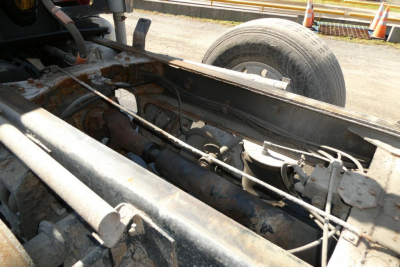 Chassis and frame of a 2000 Mack RD688S dump truck showing driveline components and a spare wheel in background.