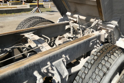 Dump truck chassis and dump bed hinge area showing heavy-duty frame and axles under a Mack RD688S.