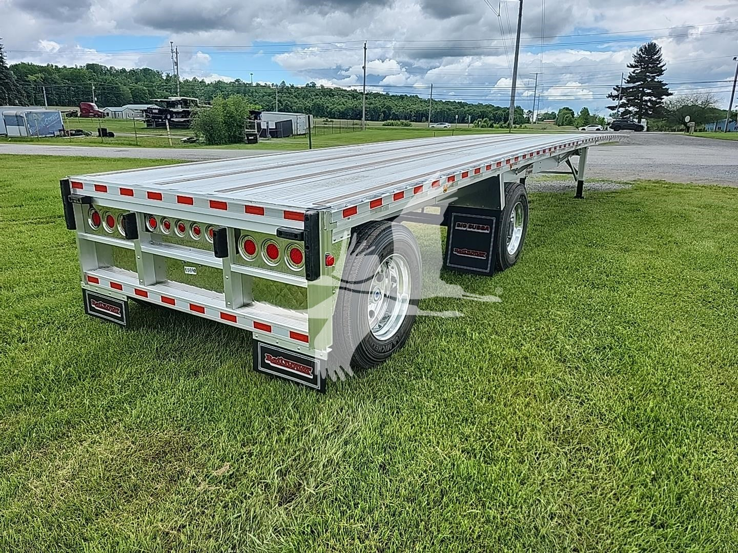 Flatbed trailer shown from rear-right side; aluminum deck, dual rear axle with round taillights, safety reflectors, and mudflaps; visible Vin/stock not on image.