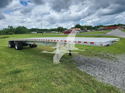 Flatbed trailer in field showing aluminum platform and dual rear axles with support legs extended.