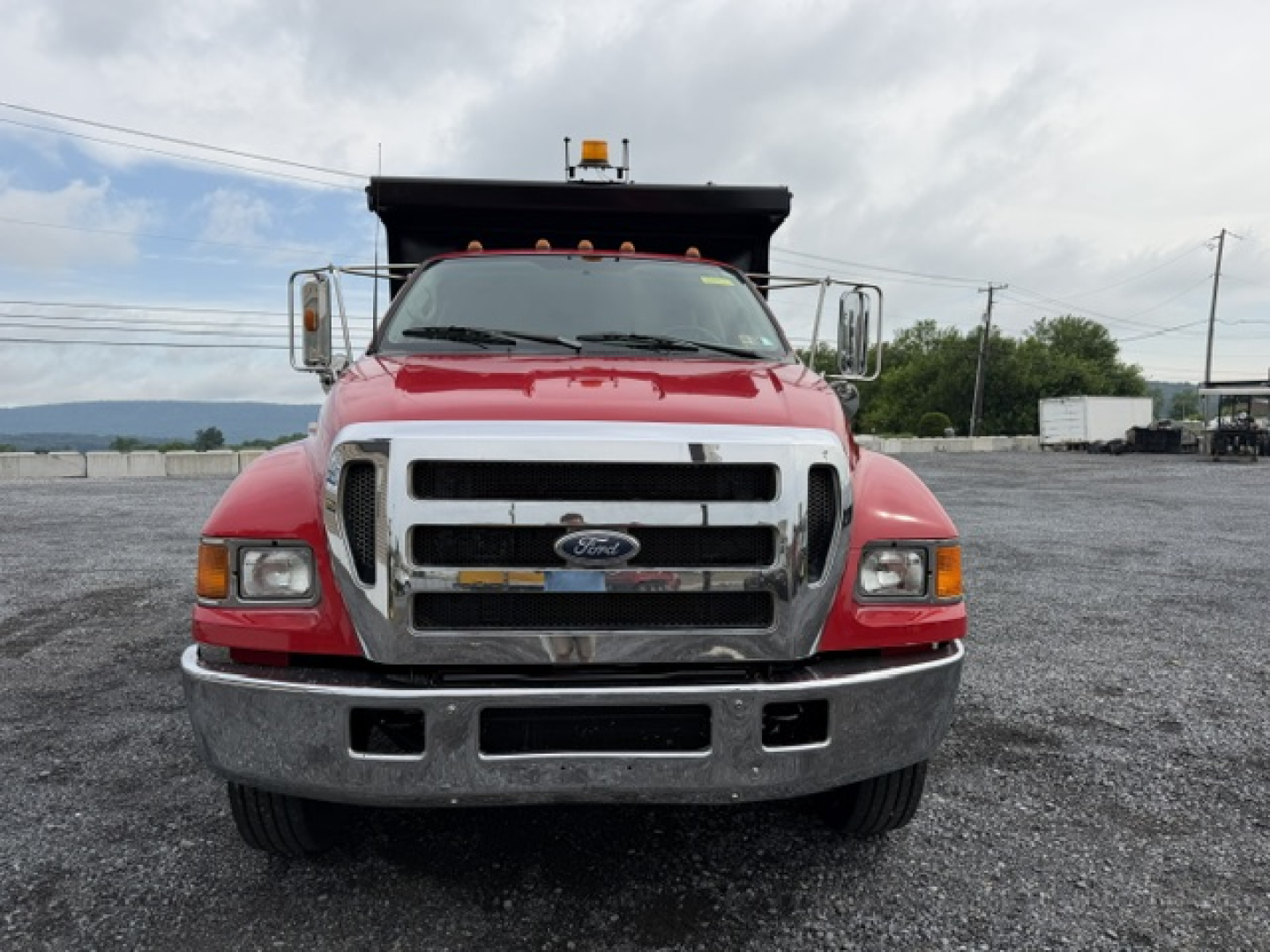 Front view of a red 2006 Ford F-750 dump truck with chrome grille, bumper, and headlights; shows large truck bed in background.