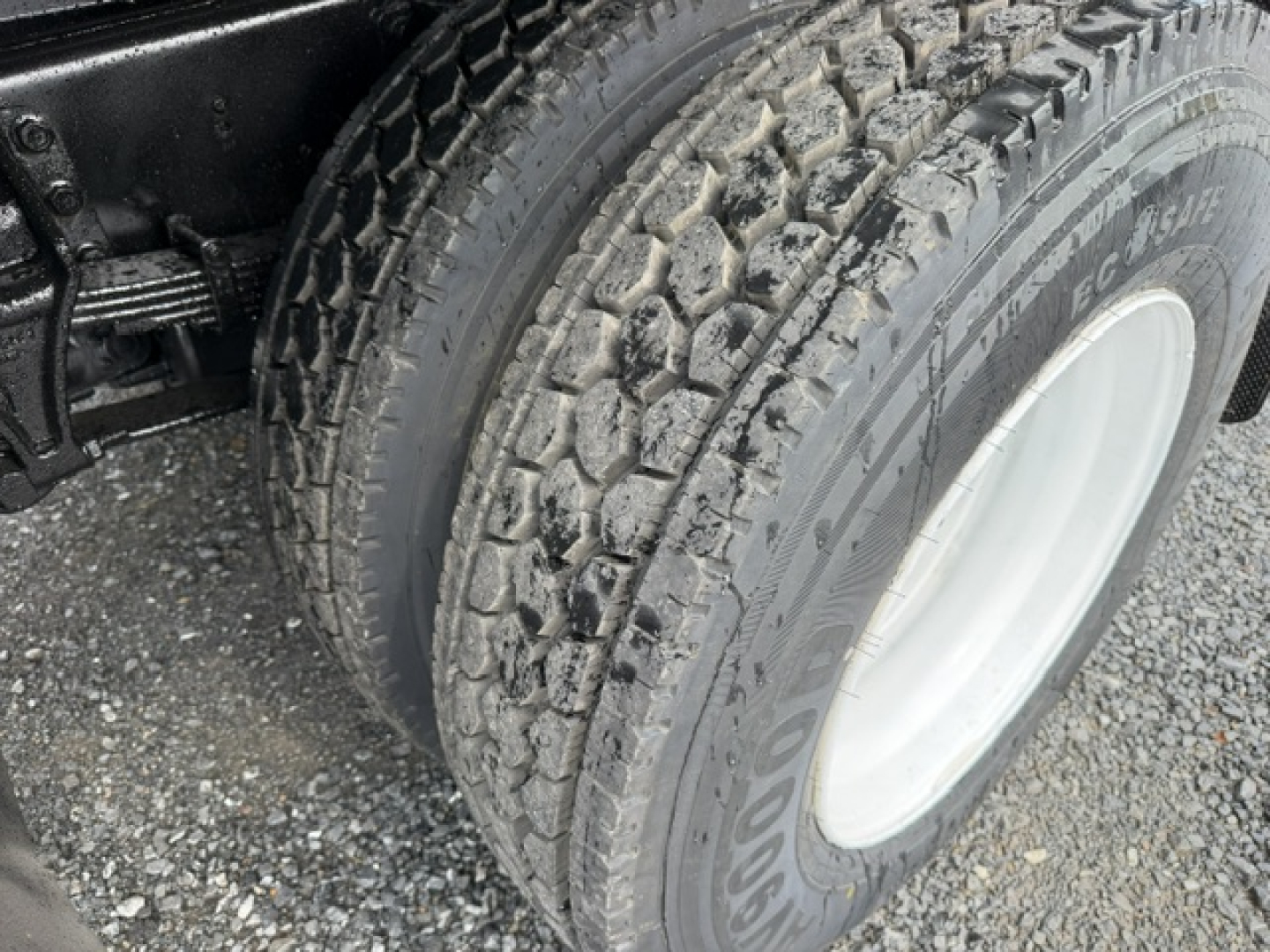 Ford F750 dump truck front wheel and tire close-up, dual rear axle, muddy tread on tire.