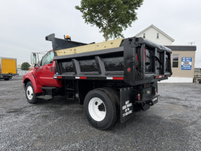 Dump truck bed and cab of a red 2006 Ford F750 with a black dump bed, rear view showing tailgate, wooden side panel, and white wheels.